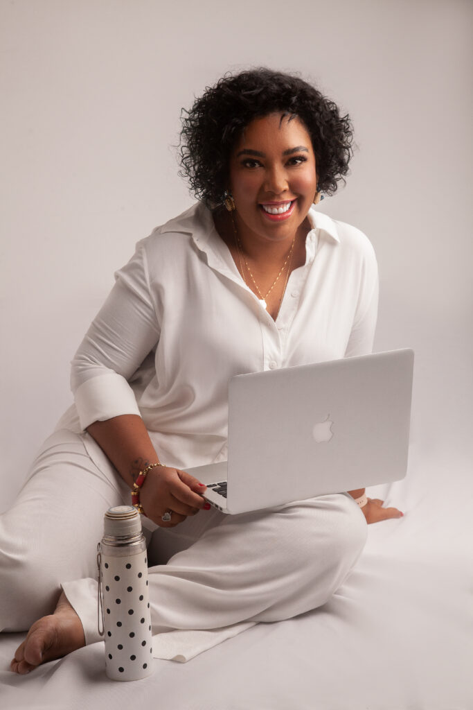 Dani Monteiro, vestida de branco, sentada no chão com um notebook no colo